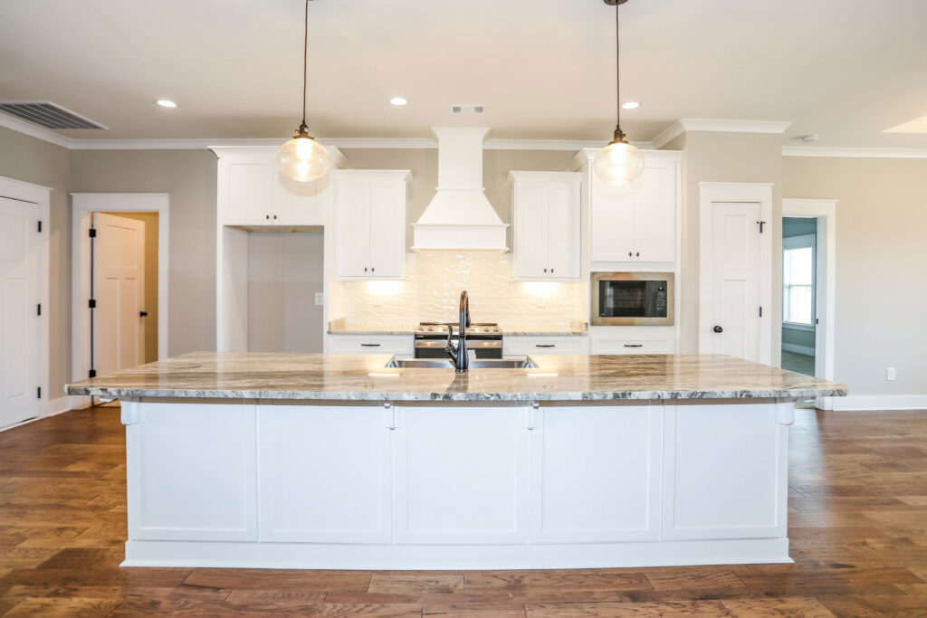 Open-concept kitchen with granite countertop island and white cabinets with pendant lighting