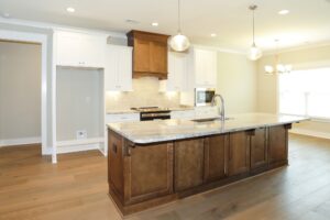 White kitchen cabinets with wood island, matching wood range hood, stone countertops, pendant lights, and open residential kitchen layout.